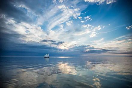 HD desktop wallpaper of a sailboat gliding on calm ocean waters under a dramatic sky filled with clouds, reflecting on the water’s surface.