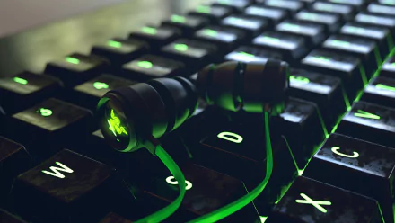 Close-up of Razer earbuds resting on a backlit keyboard, featuring glowing green keys, highlighting technology and gaming aesthetics in an HD PC desktop wallpaper style.