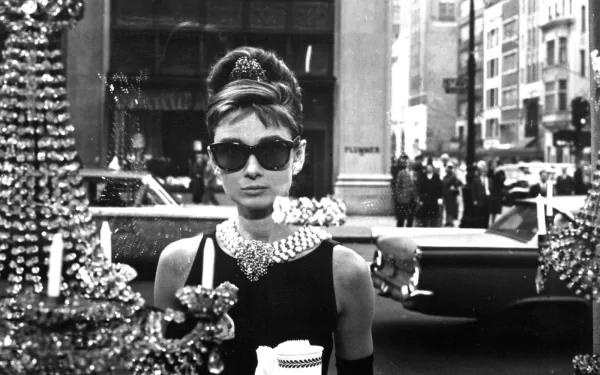 Audrey Hepburn, iconic celebrity, captures timeless elegance in this HD wallpaper. She stands confidently in black and white, adorned with stunning jewelry against a city backdrop.