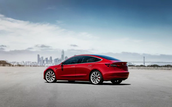 HD desktop wallpaper featuring a red Tesla Model 3 by Tesla Motors with an urban skyline in the background.