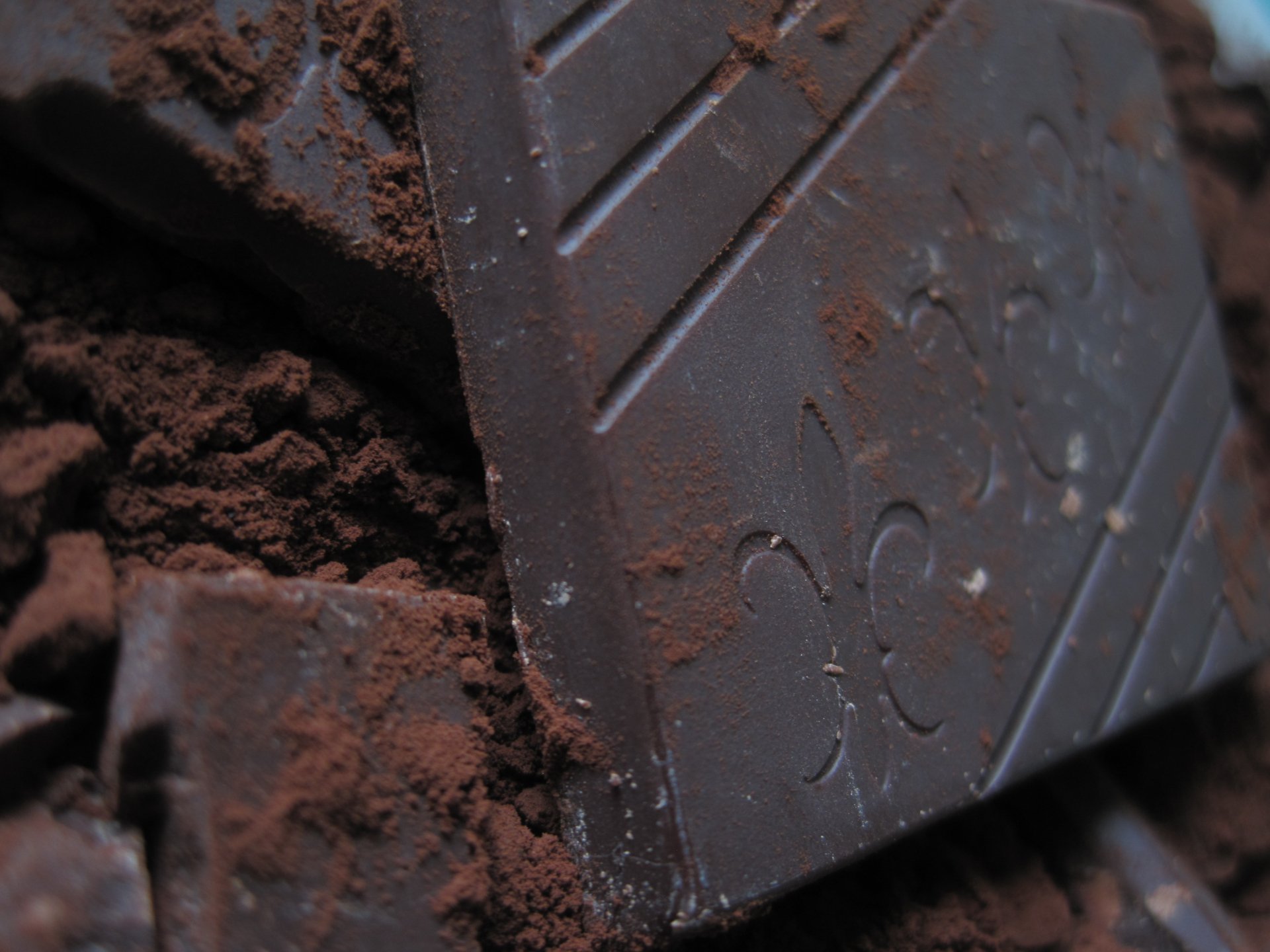 Close-up of rich chocolate pieces resting on cocoa powder, creating a tempting food-themed HD desktop wallpaper and background.