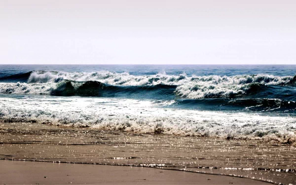 A serene beach scene featuring gentle waves crashing onto the shore, captured in high definition. This beautiful nature wallpaper invites tranquility and relaxation.