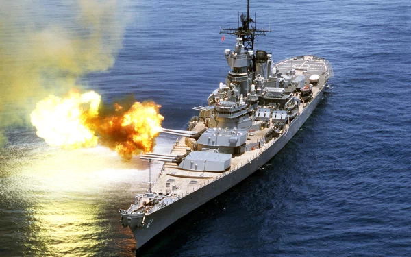 HD desktop wallpaper of the military warship USS Iowa (BB-61) in action, with its main guns firing over the ocean.