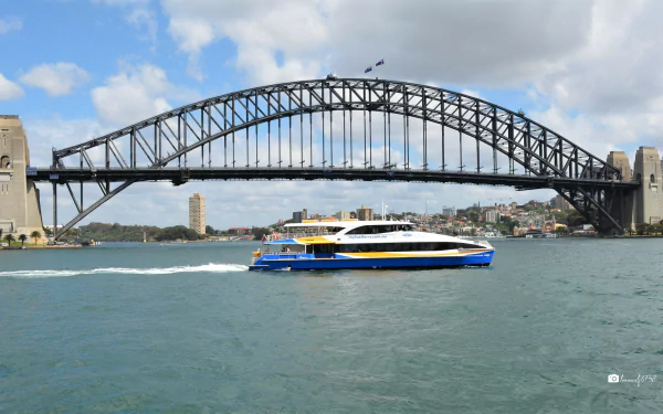 Catamaran ferry crossing Sydney Harbour in Australia beneath the Sydney Harbour Bridge — bright 2K Quad HD PC desktop wallpaper and background.