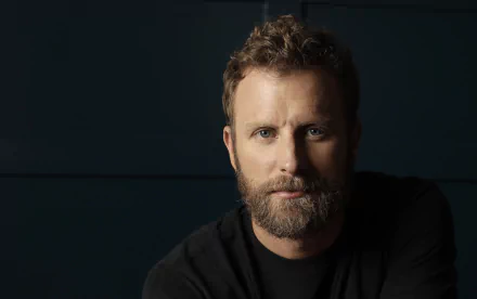 HD wallpaper featuring a portrait of a bearded man in a black shirt against a dark blue background.