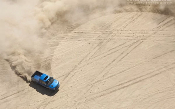 HD PC desktop wallpaper featuring a blue Ford Raptor creating tire marks and kicking up dust on a sandy terrain.