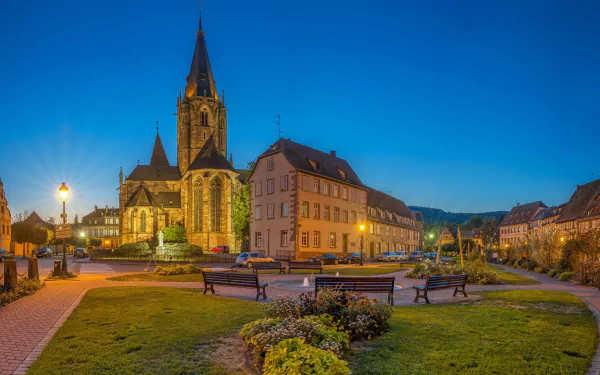HD PC desktop wallpaper of a man-made village featuring a church with a tall steeple, surrounded by historic buildings and a well-lit town square at dusk.