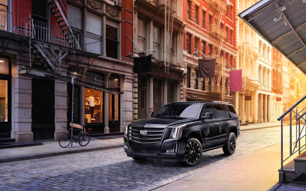 Black Cadillac Escalade SUV parked on a sunlit cobblestone city street, 4K Ultra HD PC desktop wallpaper showcasing a luxury Cadillac vehicle.