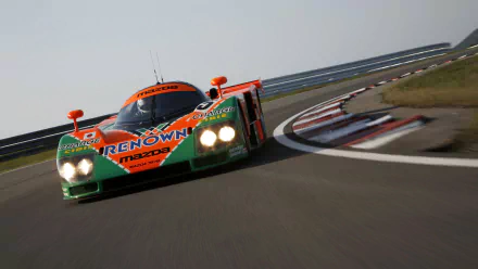 Mazda 787B race car in orange-and-green Renown livery rounding a sunlit track corner — HD PC desktop wallpaper and background.