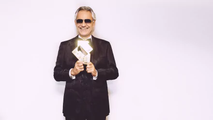 HD desktop wallpaper of Andrea Bocelli in a black suit, smiling with sunglasses, holding an award.