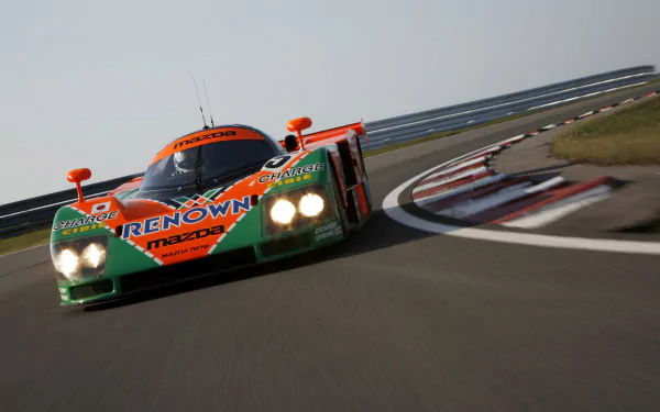 Mazda 787B race car in orange-and-green Renown livery rounding a sunlit track corner — HD PC desktop wallpaper and background.