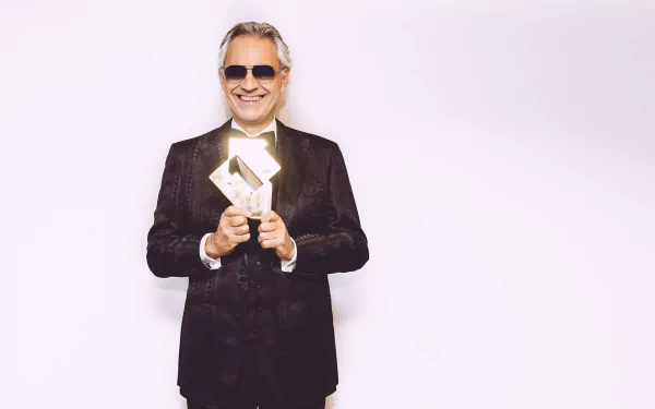 HD desktop wallpaper of Andrea Bocelli in a black suit, smiling with sunglasses, holding an award.