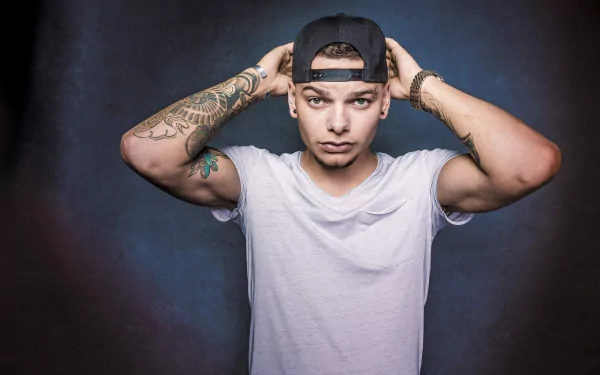 HD desktop wallpaper featuring a poised individual adjusting a baseball cap, with visible tattoos, set against a muted backdrop.