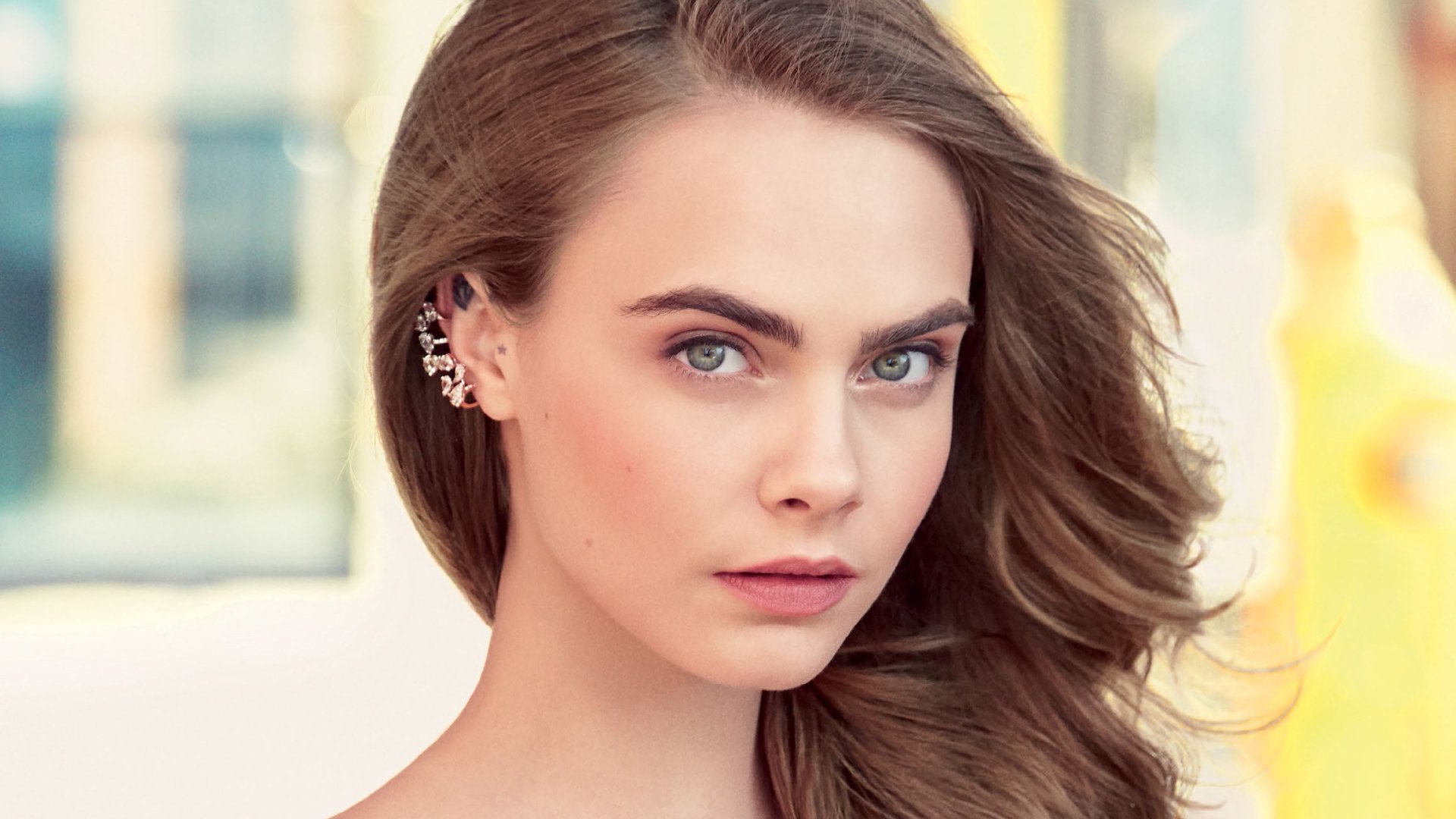 HD PC desktop wallpaper: close-up portrait of a celebrity (identity unspecified) with blue-green eyes, flowing brown hair and decorative ear cuffs against a soft, blurred background.