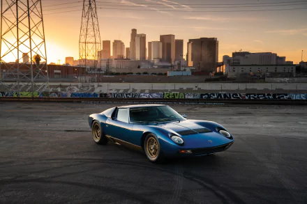 Blue Lamborghini Miura on an industrial lot at sunset with a city skyline behind — HD desktop wallpaper of the classic sports car.
