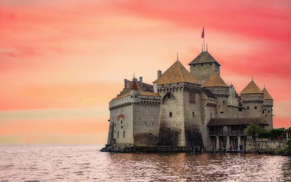 Chateau de Chillon, a historic castle in Veytaux, Switzerland, stands against a vibrant sunset sky over the calm waters, captured in a stunning HD desktop wallpaper.