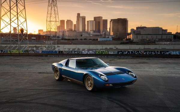 Blue Lamborghini Miura on an industrial lot at sunset with a city skyline behind — HD desktop wallpaper of the classic sports car.