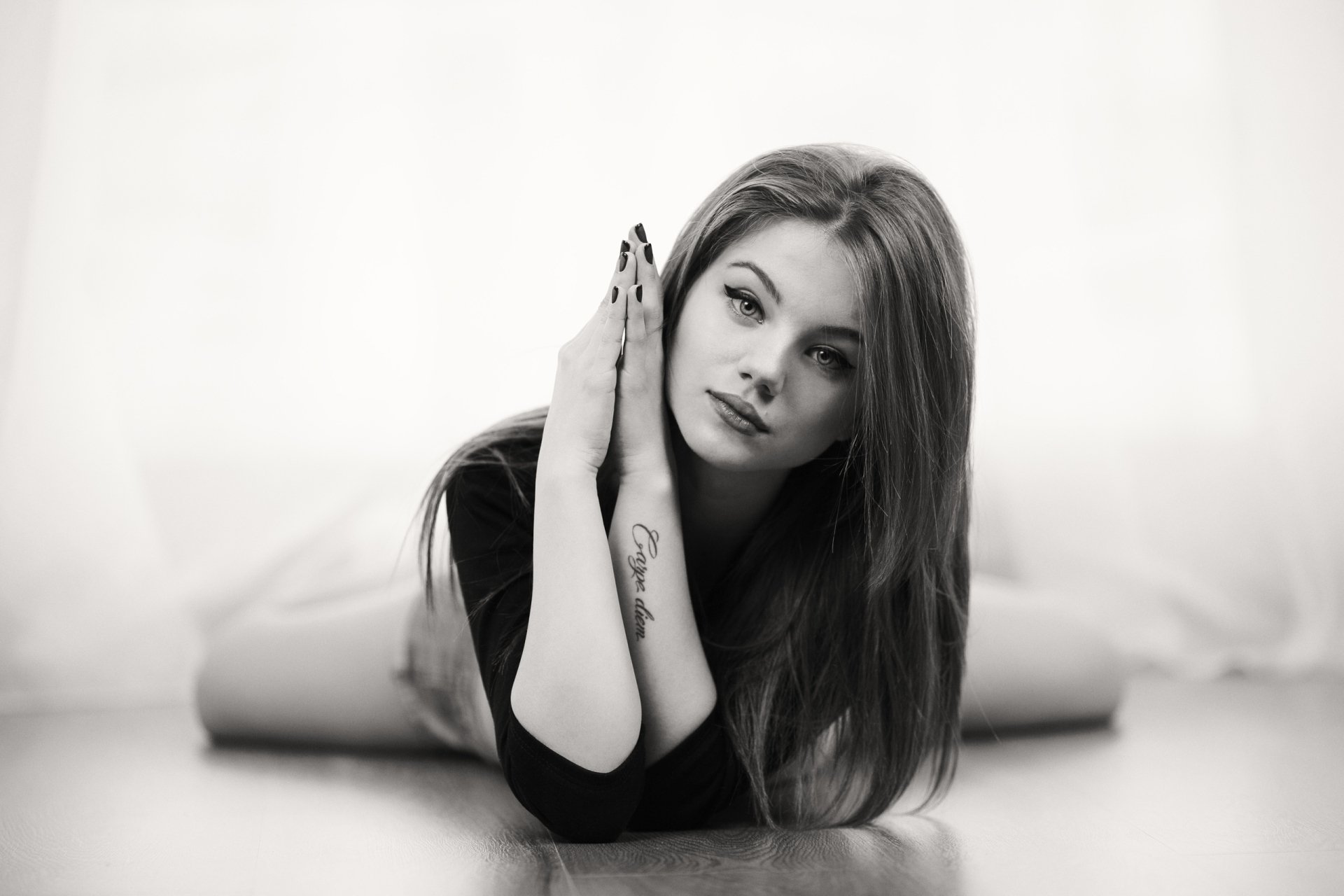 Black and white HD wallpaper of a long-haired woman model with lipstick, lying down and gazing directly with an intense stare.