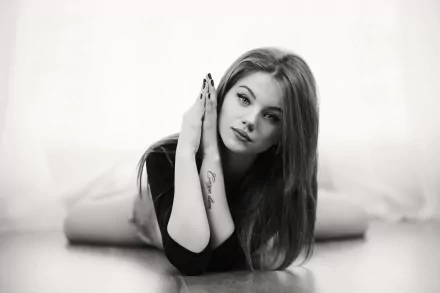 Black and white HD wallpaper of a long-haired woman model with lipstick, lying down and gazing directly with an intense stare.