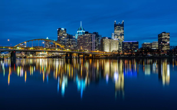 HD desktop wallpaper showing Pittsburgh's illuminated skyscrapers and bridges at night, with vibrant reflections on the calm river in the USA cityscape.