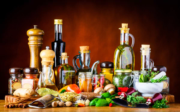 Still life of bottles of oil, jars, herbs, spices and fresh produce on a wooden table — 5K Ultra HD PC desktop wallpaper/background.