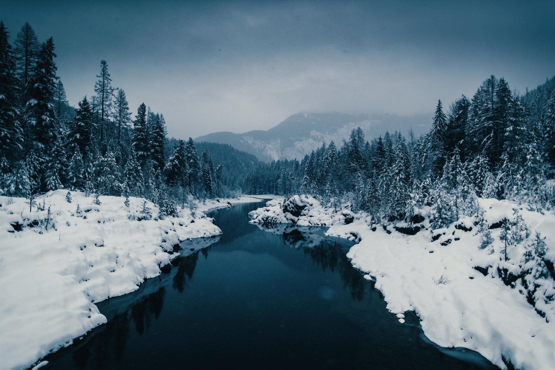 HD desktop wallpaper showcasing a serene winter lake surrounded by snow-covered trees and mountains under a cloudy sky in a natural landscape.