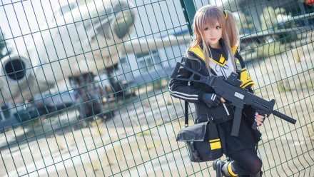 HD PC desktop wallpaper of a woman cosplaying UMP9 from Girls' Frontline, holding a submachine gun and posing by a chain-link fence with blurred aircraft in the background.