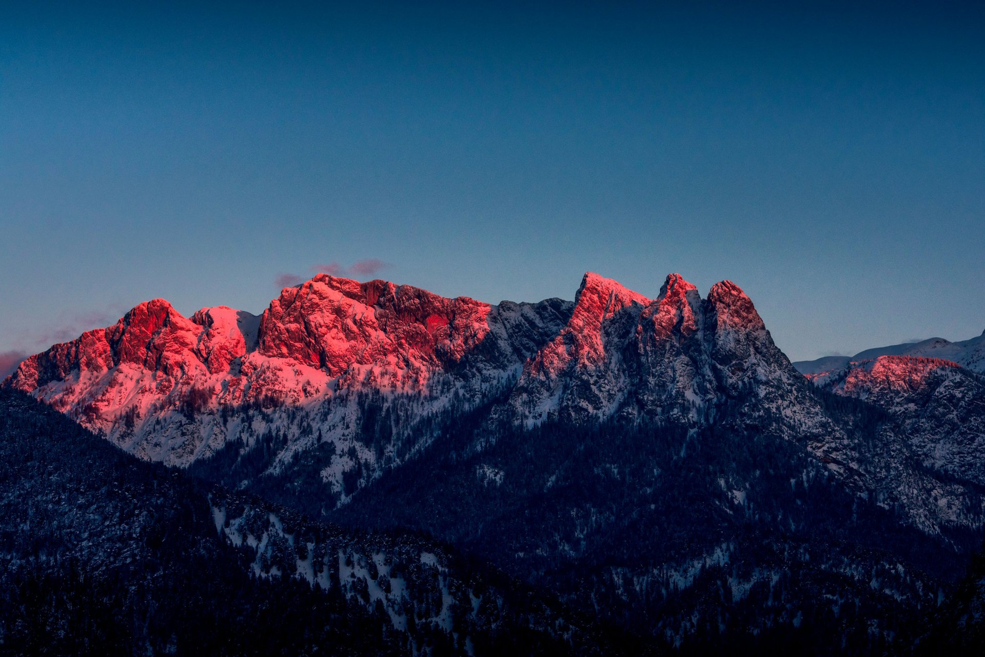 HD PC desktop wallpaper featuring a mountain range bathed in warm, reddish light against a clear blue sky, showcasing stunning natural beauty.