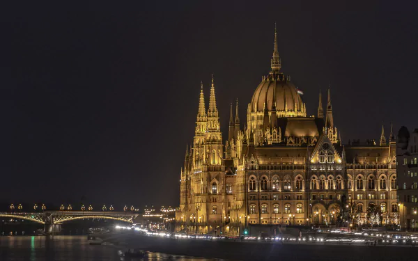 Night view of the illuminated Hungarian Parliament Building in Budapest, Hungary, showcasing its intricate architecture along the river, captured in HD quality.