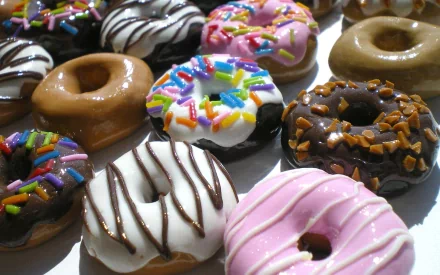HD desktop wallpaper featuring an assortment of colorful doughnuts, topped with rainbow sprinkles, chocolate drizzle, and various icing flavors.