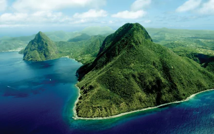 HD desktop wallpaper showcasing the lush green mountains and vibrant ocean of Saint Lucia under a bright, partly cloudy sky.