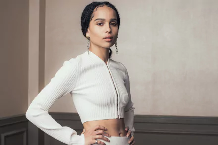 HD desktop wallpaper of American actress Zoë Kravitz with black hair, brown eyes, and dangling earrings, posing confidently against a neutral background.